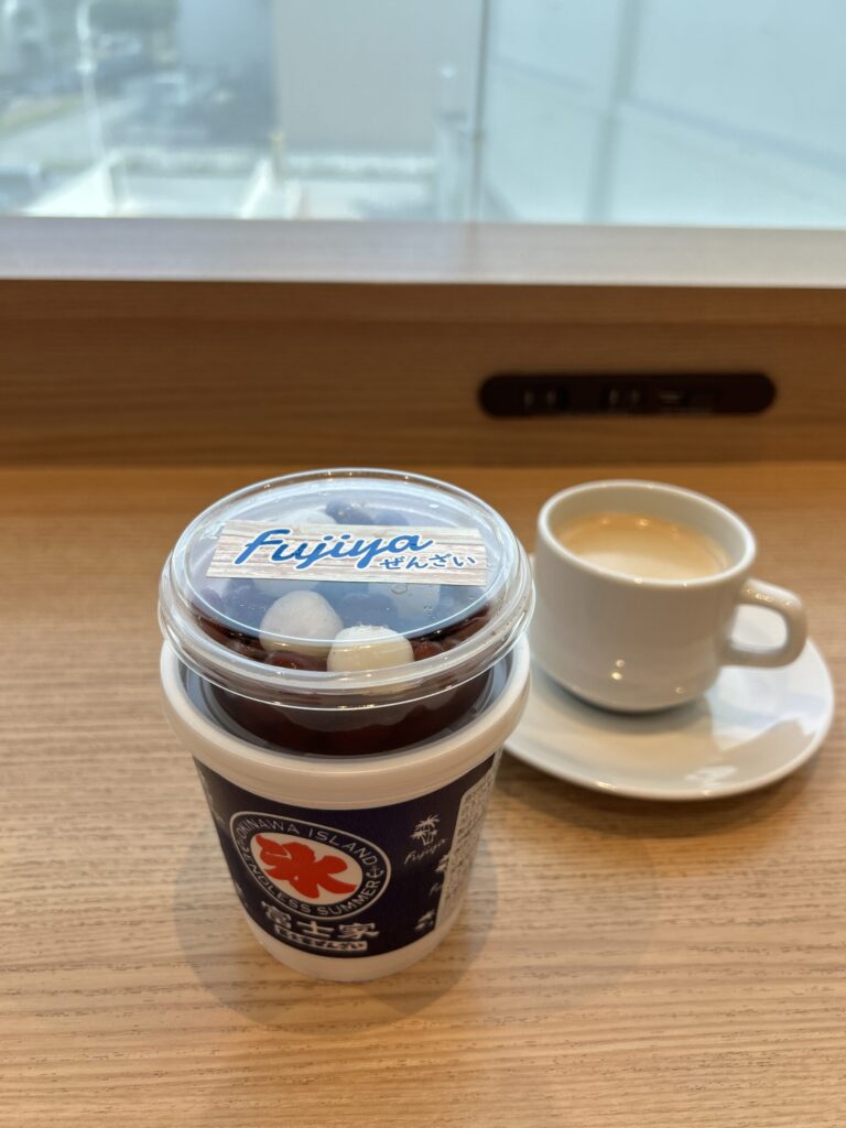 那覇空港のラウンジで、テイクアウトした富士家の沖縄ぜんざいとブラックのホットコーヒーがテーブルに並んでいる様子。