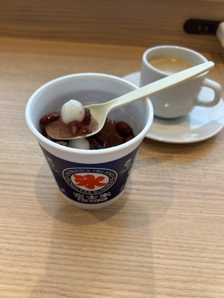 那覇空港の富士家（ふじや）沖縄ぜんざい。透明なカップに入った茶色の煮汁凍結氷と大粒の金時豆、白い白玉のクローズアップ写真。